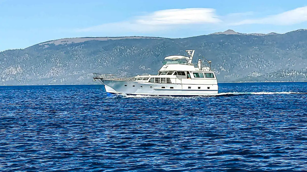 The white Bleu Wave motor yacht cruising on deep blue Lake Tahoe with the east shore hills behind