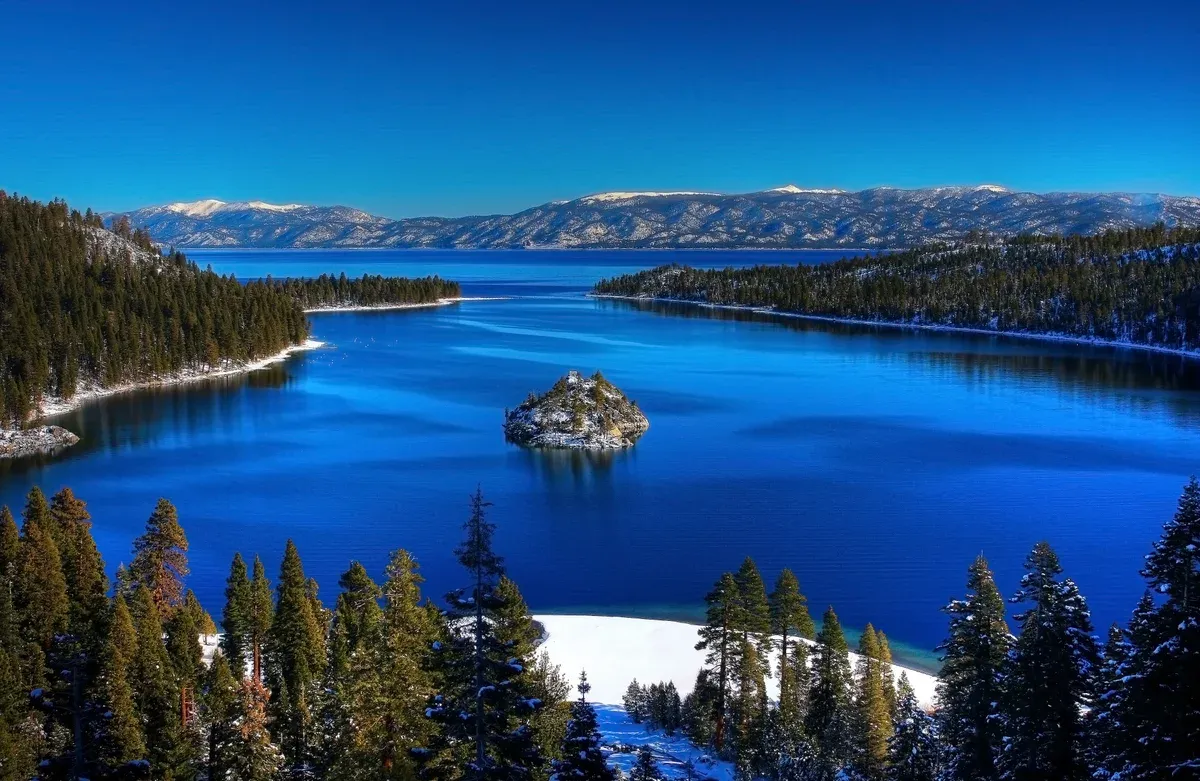 Fannette Island in deep blue Emerald Bay with snow patches on the shore and the open lake beyond