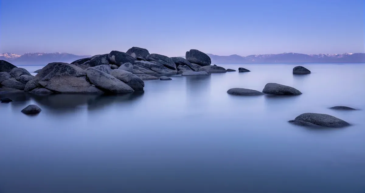Smooth granite boulders in calm blue Lake Tahoe water in soft low light