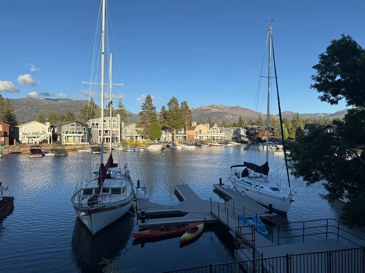 Sailboats moored at private docks in a South Lake Tahoe marina channel with lakefront homes behind