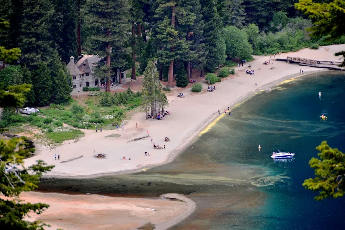 Vikingsholm among the pines at the head of Emerald Bay above a sandy beach, with a small boat in the shallows